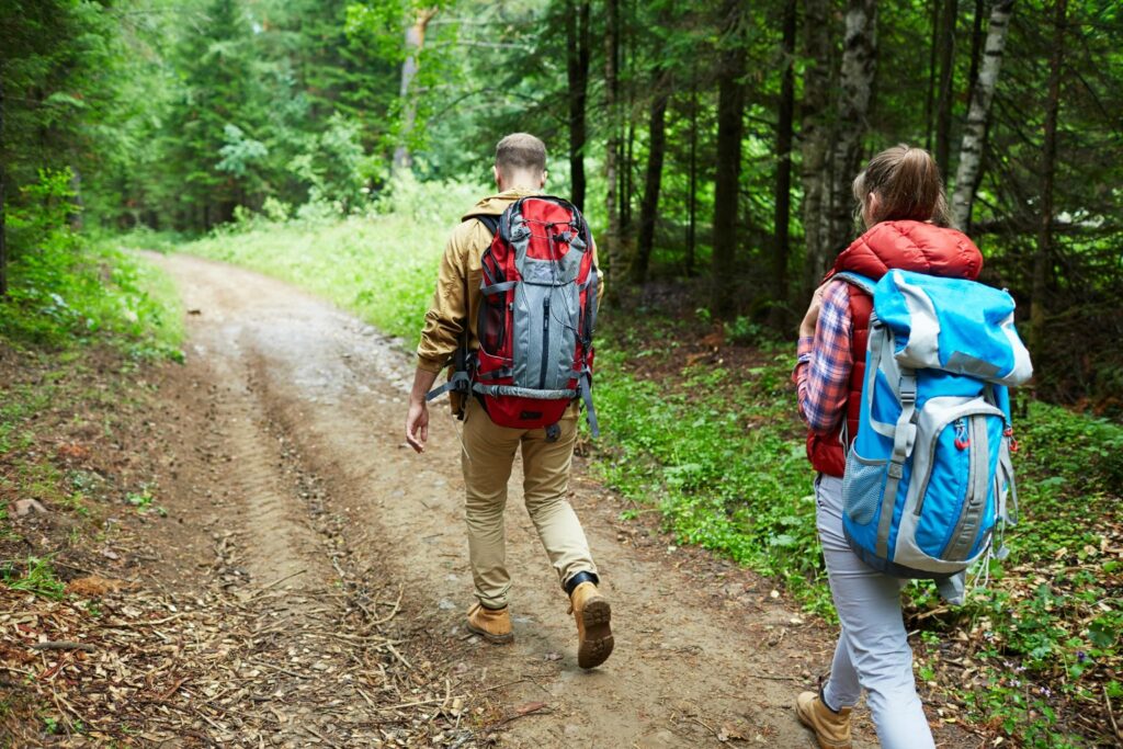 Man and woman with backpacks walking down forest path